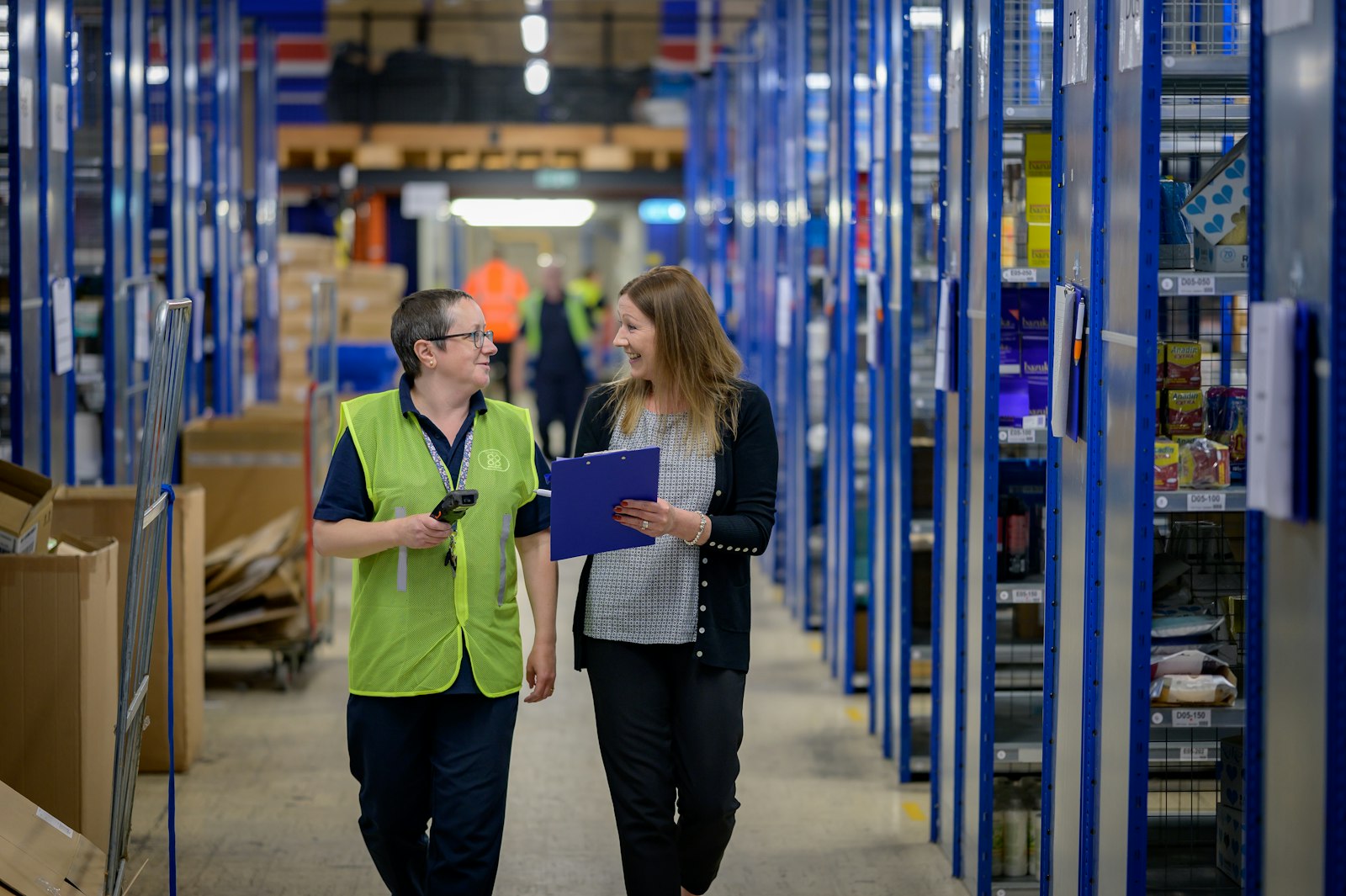 Two workers walking a warehouse aisle between blue racking