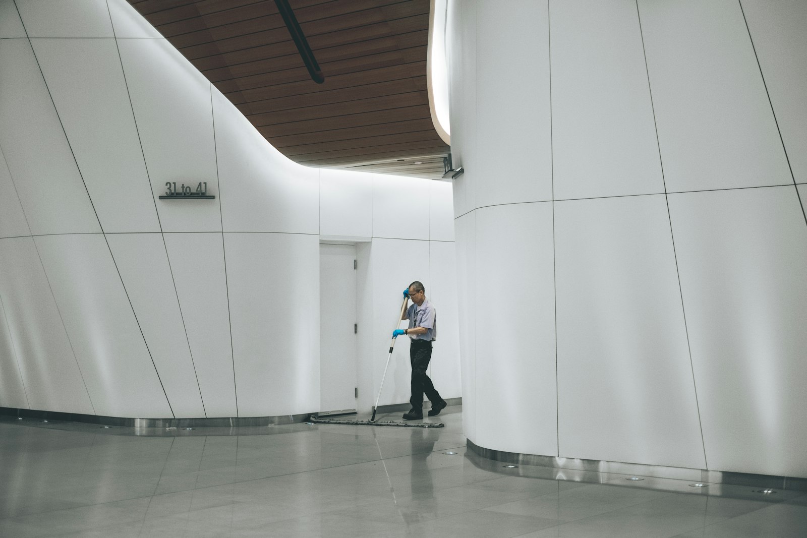 Custodian cleaning a hard floor beside a white wall