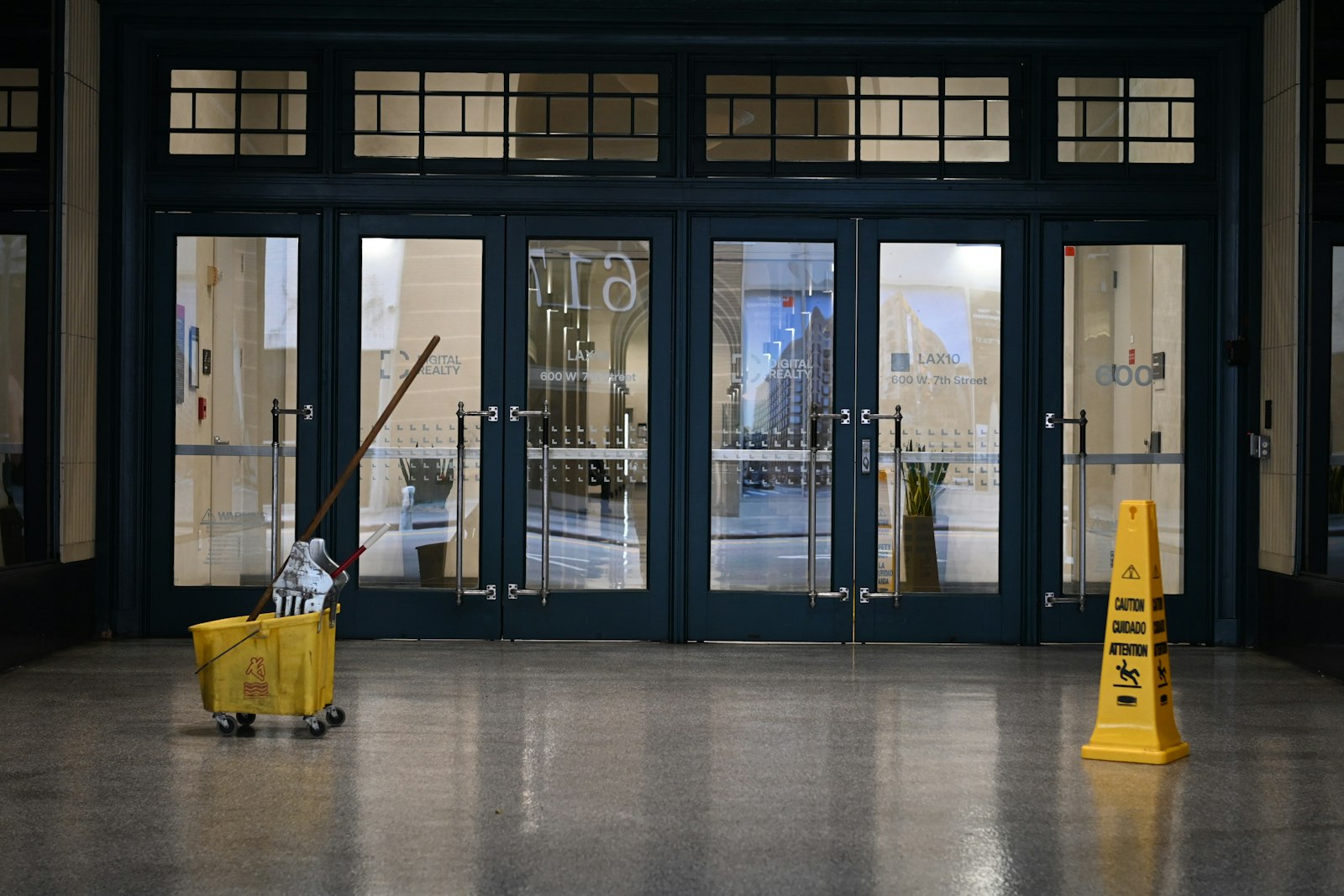 Mop bucket and wet-floor sign inside a glass lobby entrance