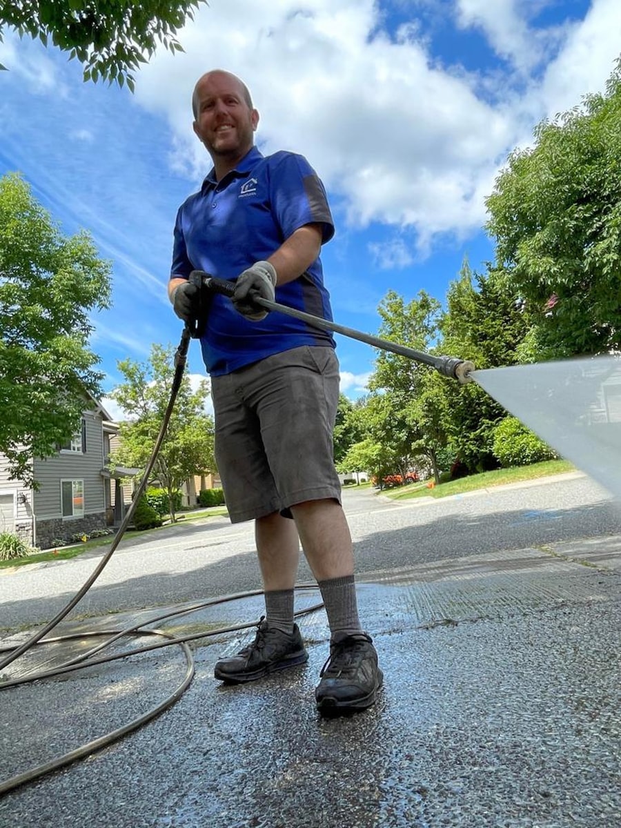 Technician pressure washing a driveway with a wand