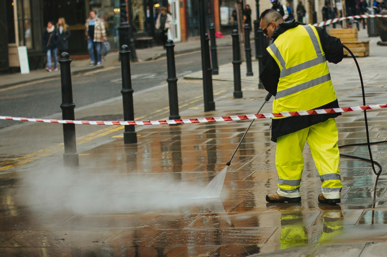 Worker in a hi-vis jacket pressure washing a paved plaza