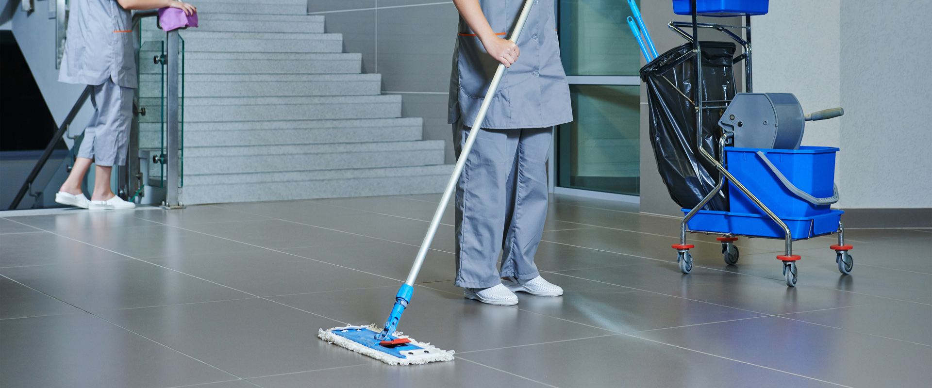 Cleaning crew member with a mop cart on a tiled lobby floor